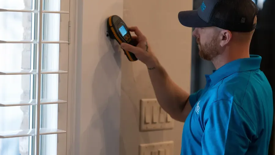 Technician checking a wall with a pinless moisture meter during restoration