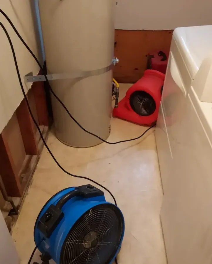 Drying fans beside a water heater and an opened utility-room wall