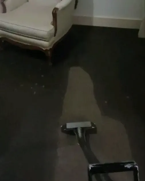 Extraction wand drawing water from a dark floor beside a wall corner