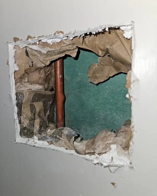 Opening cut into an interior wall to expose a copper pipe