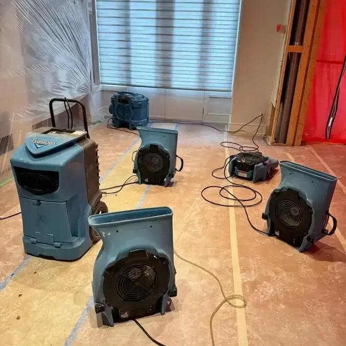 Air movers and a dehumidifier arranged on an exposed interior subfloor