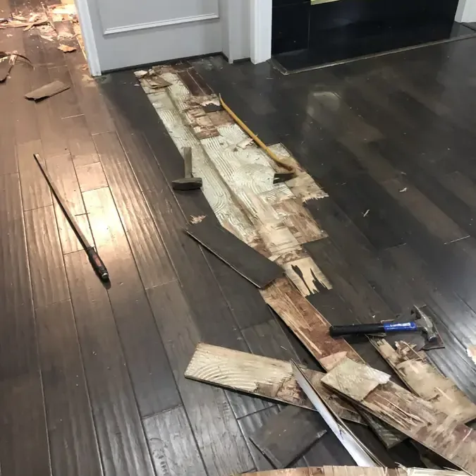 Damaged wood flooring removed along a doorway to expose the layers beneath