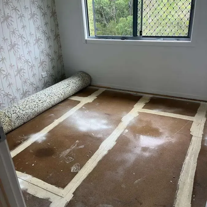 Carpet rolled back beside a window to expose a wet floor