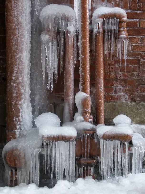 Ice coating exposed plumbing pipes against a brick wall