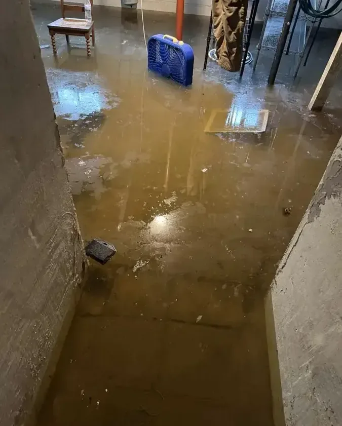 Muddy standing water covering a basement floor beside stored equipment