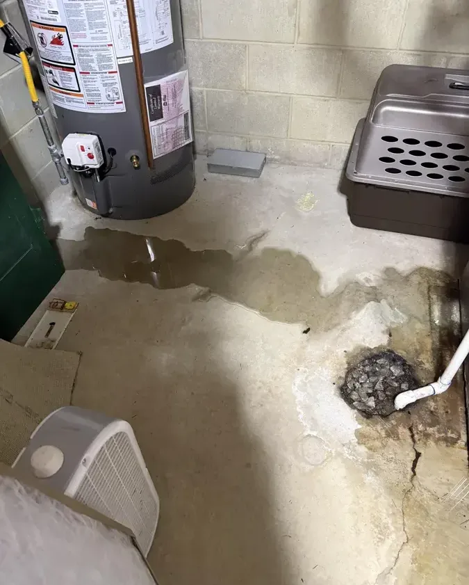 Water spreading across a basement floor from a leaking water heater toward the floor drain